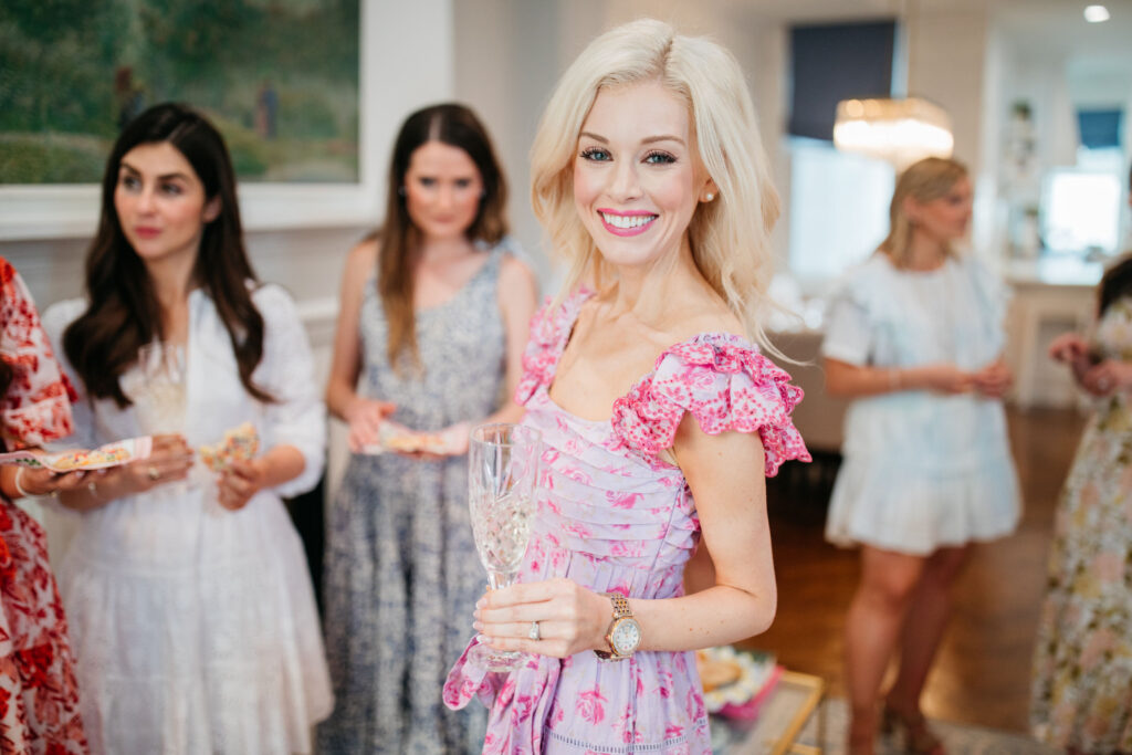 Alison Cheperdak smiling while holding a crystal glass during an elegant indoor gathering with guests, demonstrating modern hosting and social etiquette.